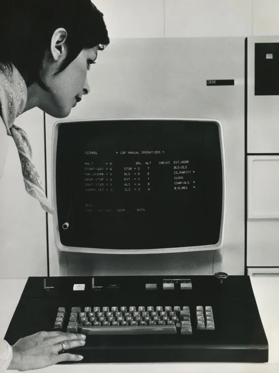 "Das Bild zeigt eine Frau, die den Bildschirm eines alten Computers betrachtet, einen IBM System 370 Modell 115.