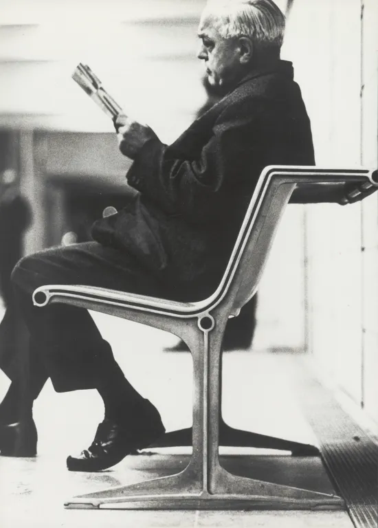 Auf dem Bild ist ein Mann in einem Anzug zu sehen, der auf einem Stuhl von Designer Friso Kramer sitzt und eine Zeitschrift liest.